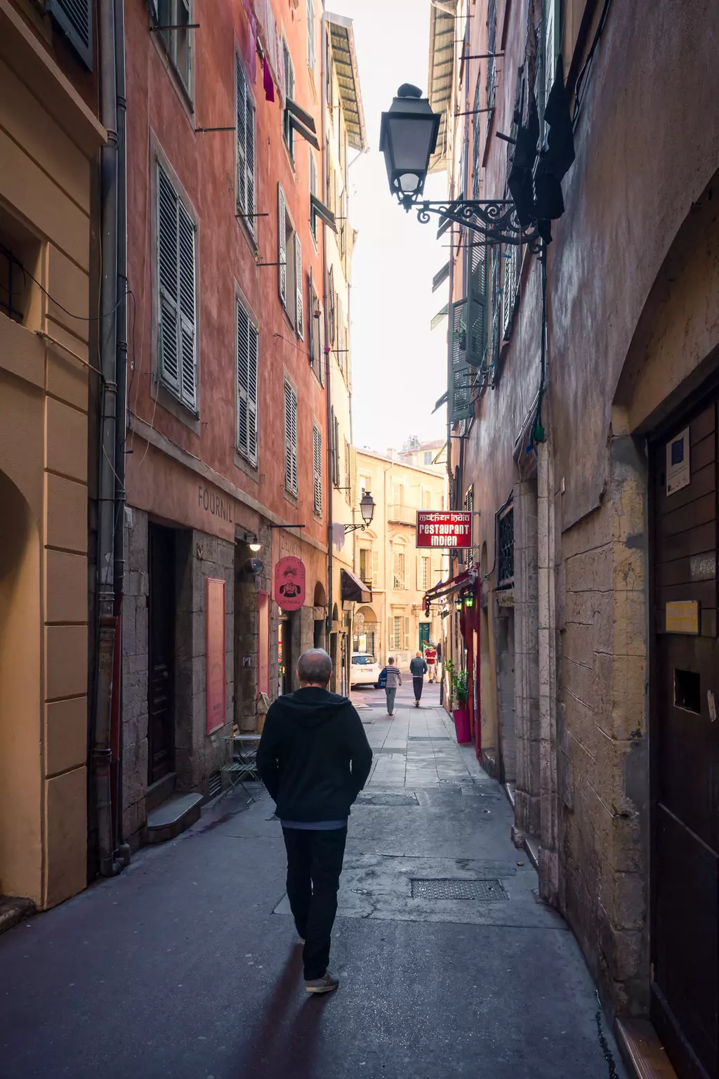 A man walks alone down a narrow alley, surrounded by colorful buildings and shops.