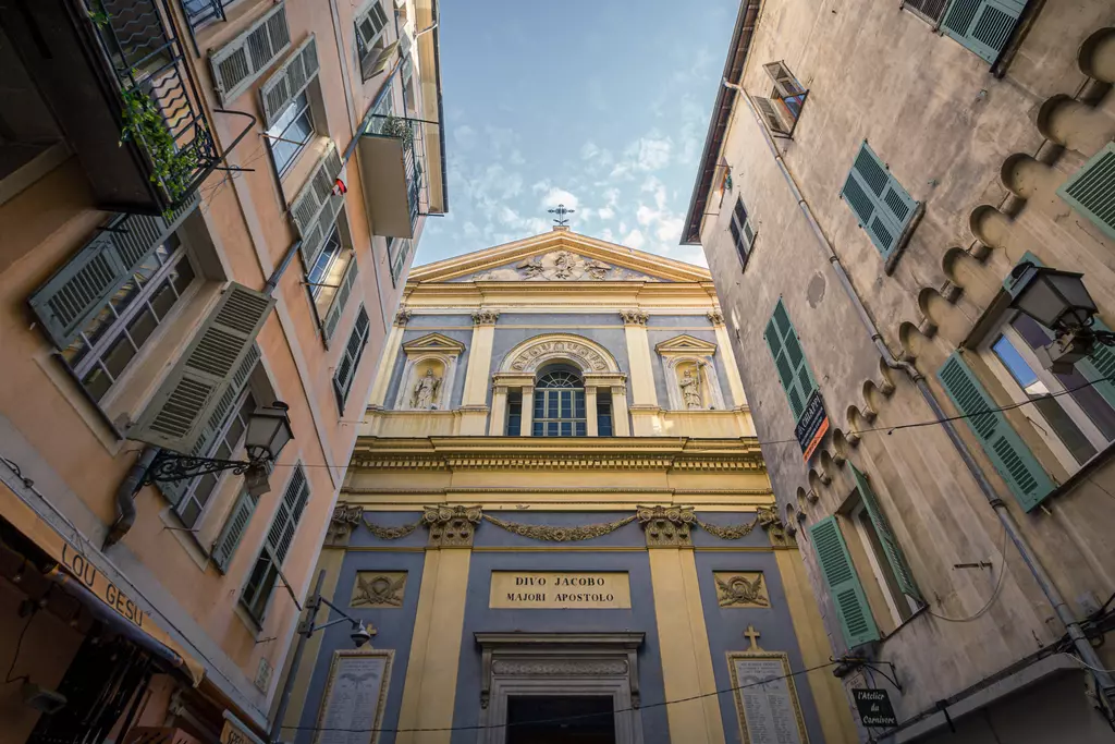 A narrow alley with colorful buildings leads to an impressive historic church featuring a blue and yellow facade.