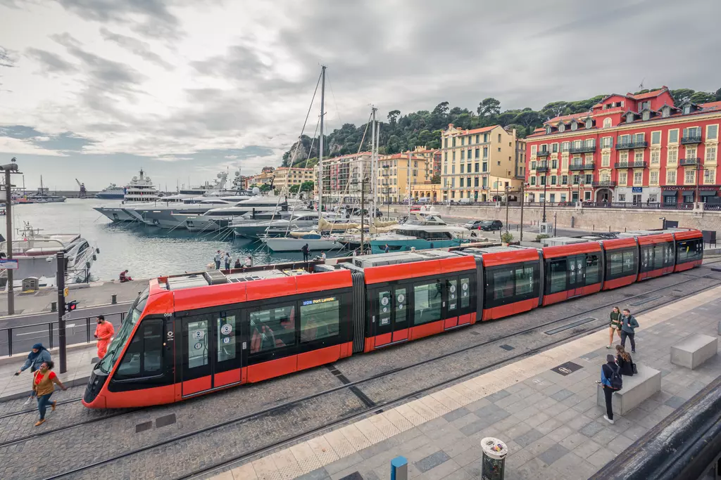 Waterfront in Nice: A red tram travels along the harbor, surrounded by colorful buildings and yachts.