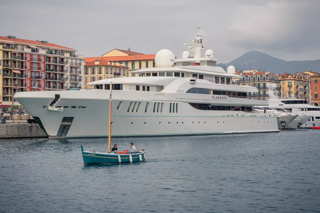 A large yacht is anchored in the water, while a small boat with two people passes nearby, surrounded by residential buildings.