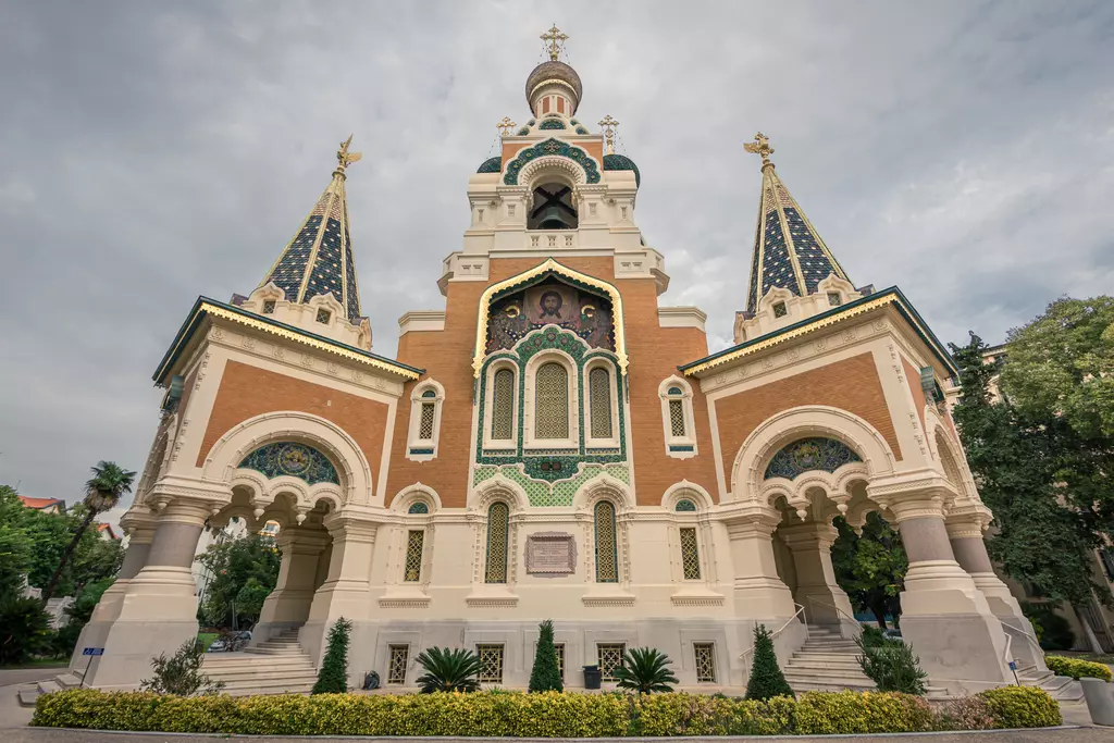 A colorful historic building with towers, golden domes, and intricate details, surrounded by lush greenery.