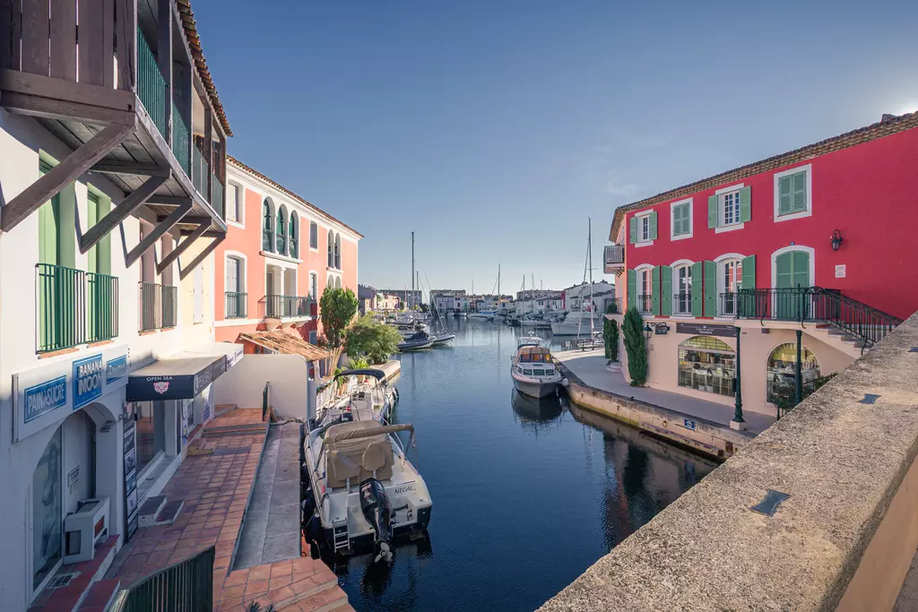 Bunte Gebäude spiegeln sich im ruhigen Kanal, an dem Boote vor Anlegestellen liegen und der sanft zwischen den Ufern fließt.