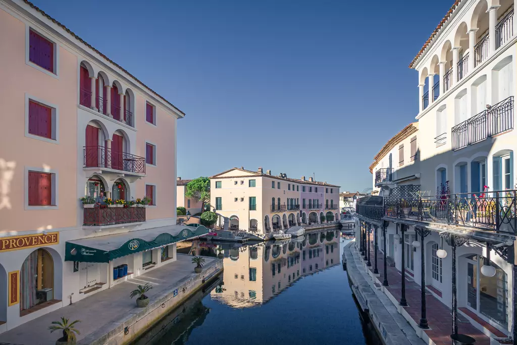 Port Grimaud: Farbige Gebäude am Kanal spiegeln sich im Wasser. Balkonverzierungen und Palmen ergänzen die malerische Szenerie.