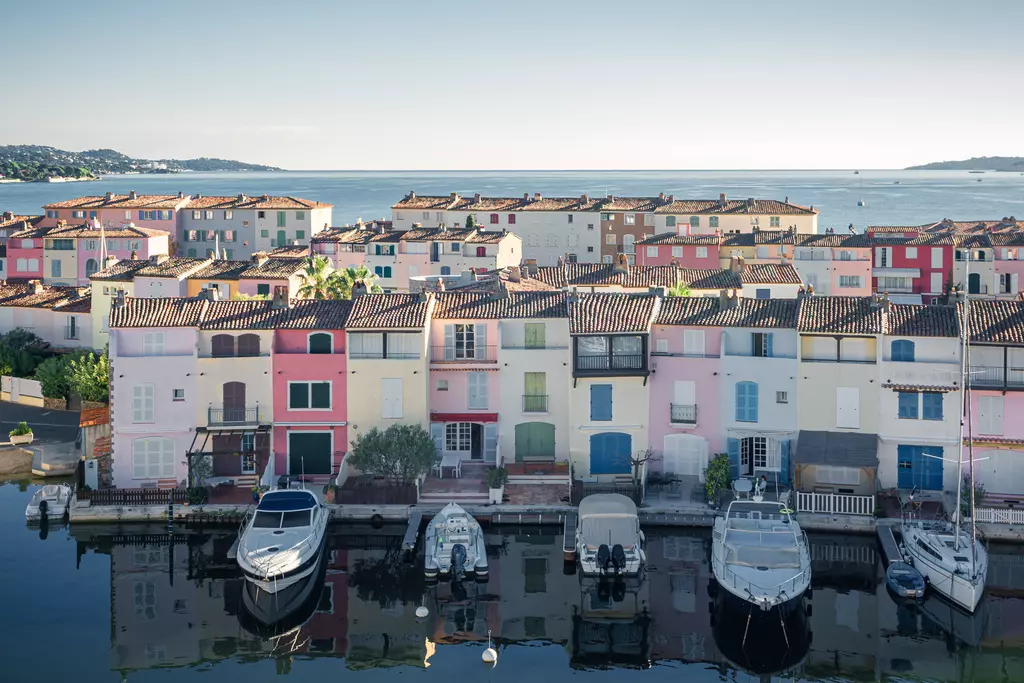 Port Grimaud: Bunte Häuser am Wasser mit Booten im Vordergrund und ruhigem Meer im Hintergrund.