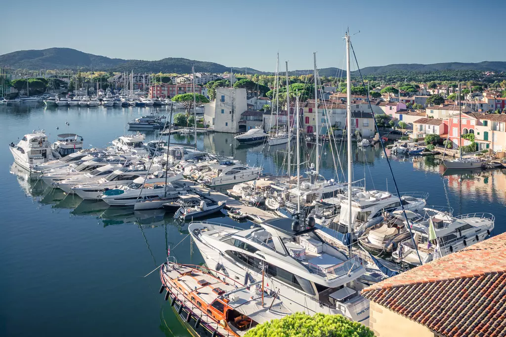 Häfen voller Yachten und Boote umgeben von bunten Häusern und grüner Landschaft im Hintergrund.