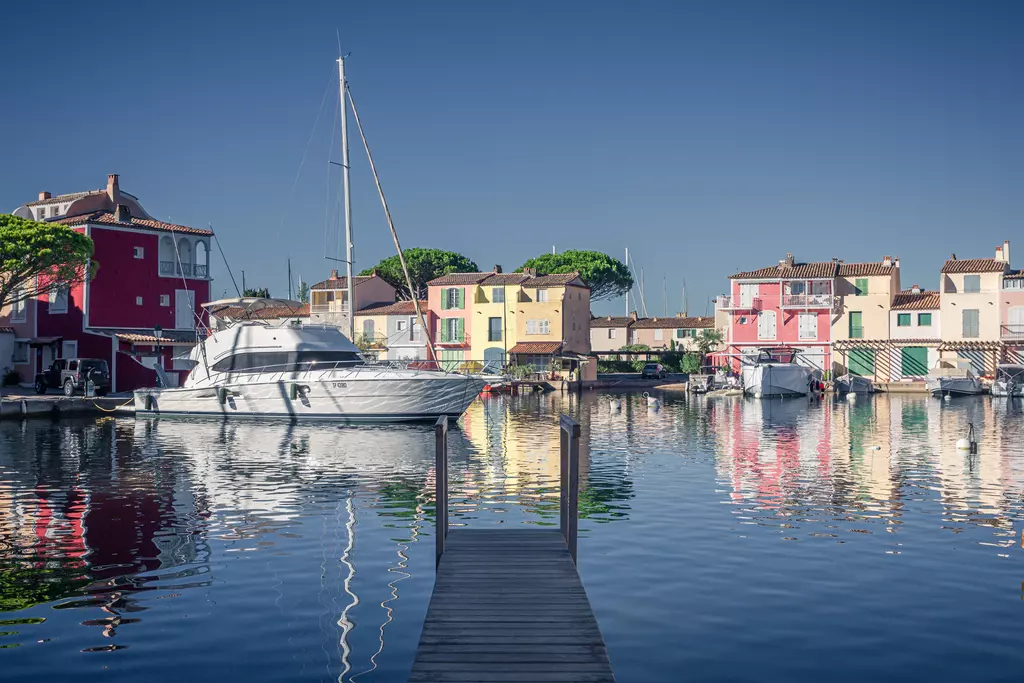 Eine Holzpier führt zu einem ruhigen Kanal, umgeben von bunten Gebäuden und einem weißen Boot, das im Wasser reflektiert wird.