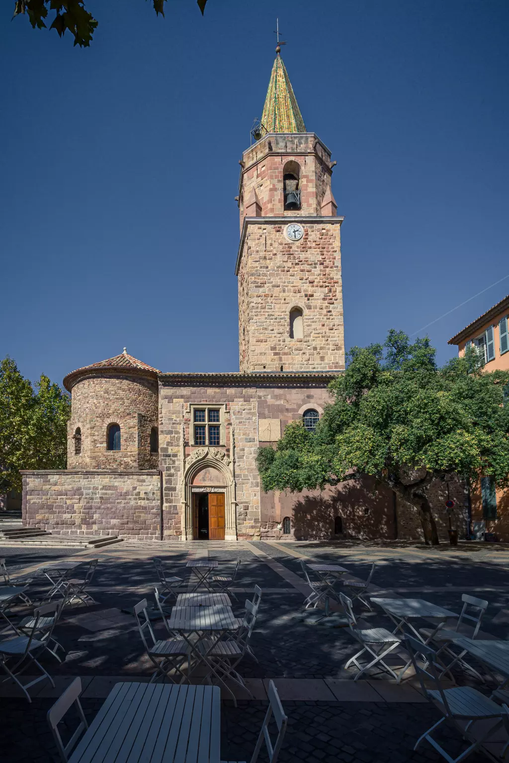 Kathedrale von Fréjus: Historisches Gebäude mit einem hohen Glockenturm, umgeben von Bäumen und weißen Tischen im Freien.