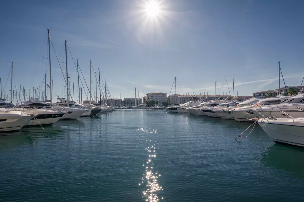 Helle marina mit vielen Yachten, die im Wasser liegen. Die Sonne strahlt über den Booten, das Wasser glitzert im Licht.