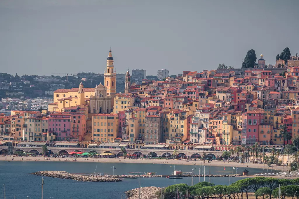 Colorful cityscape of Menton, featuring historic buildings and a waterfront promenade by the sea.