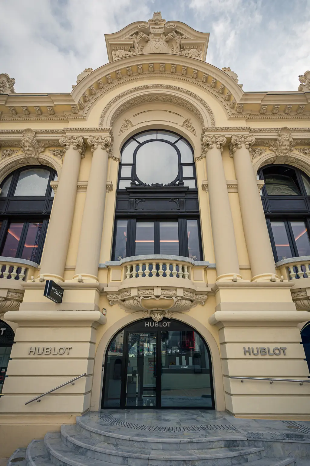 An opulent building with large windows and intricate architectural details, featuring an entrance marked by Hublot signage.