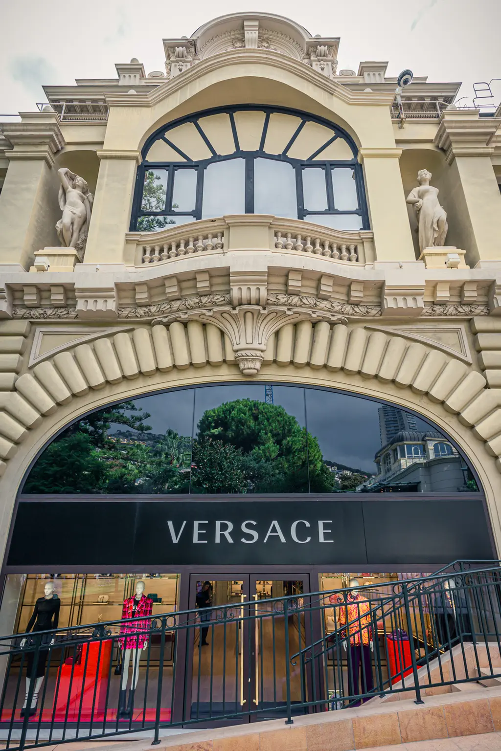 The elegant facade of a Versace store featuring sculptures and a window balcony, reflecting the surrounding environment.