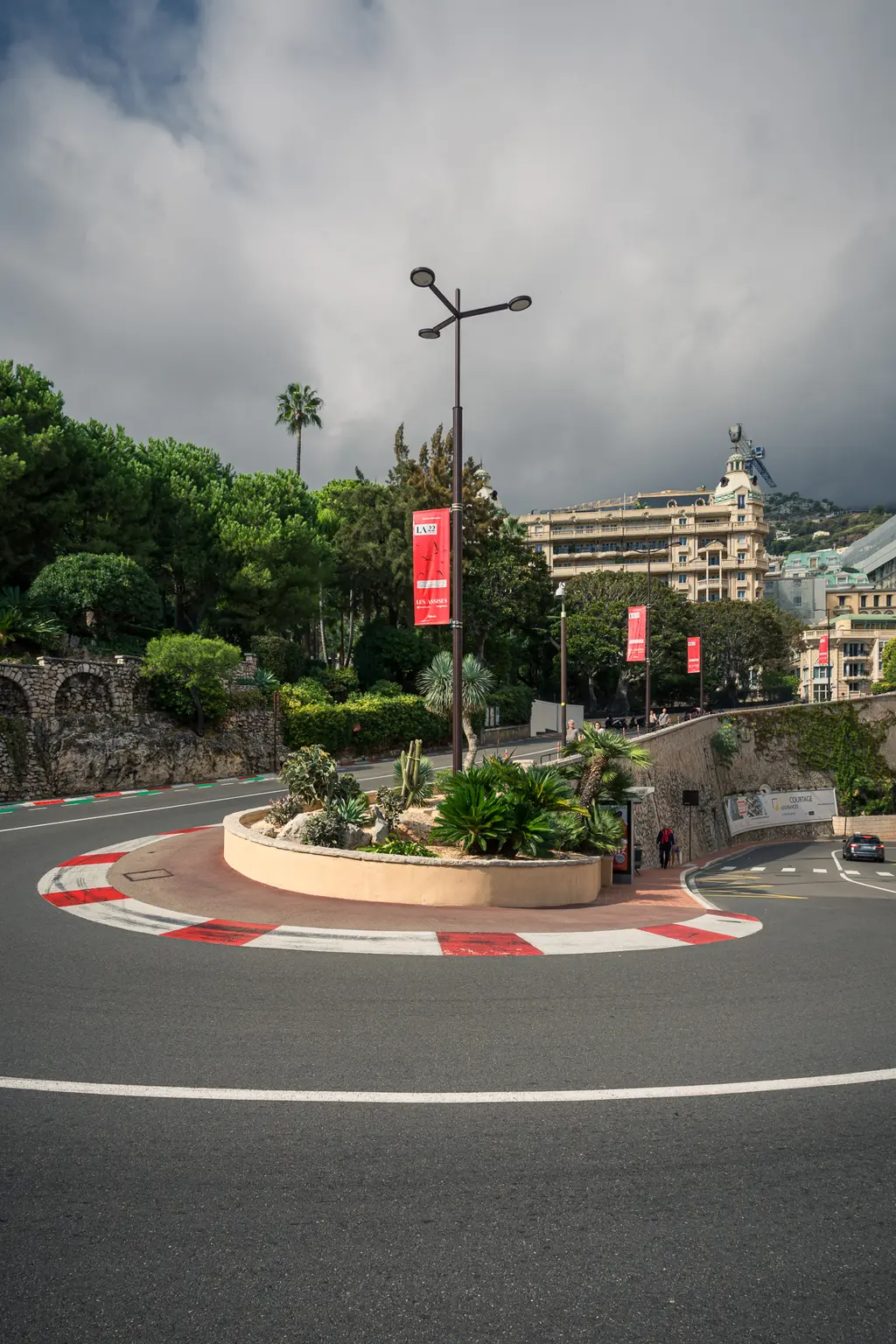 A winding road with a large roundabout, surrounded by green trees and buildings in Monaco.