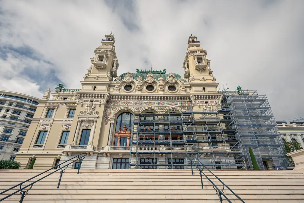 The impressive facade of a historic building with scaffolding, ascending steps, under a cloudy sky.
