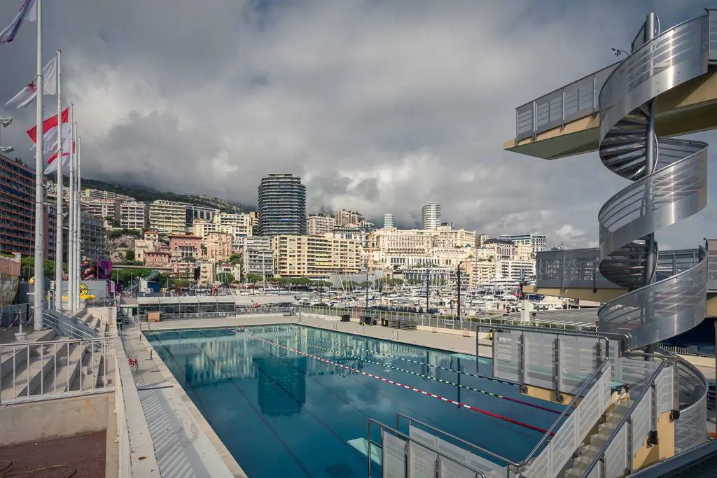 A modern swimming facility featuring a clear pool and a spiral staircase leading up to a diving platform.