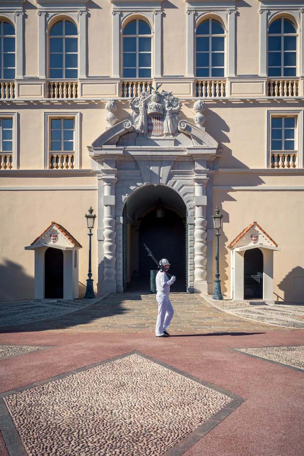 A soldier in a white uniform stands before a grand archway, flanked by two lanterns and an ornate building in the background.