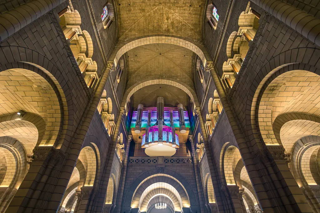 A view of the tall ceiling of a church featuring impressive arches, colorful stained glass windows, and a large organ in the background.