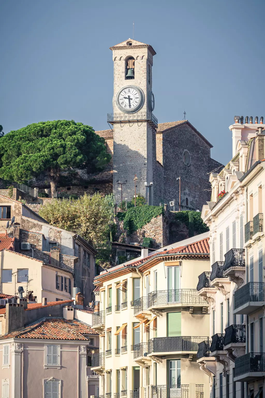 Eglise Notre-Dame d'Espérance in Cannes: Die Kirche mit Uhrturm thront über bunten Gebäuden und grünen Bäumen.