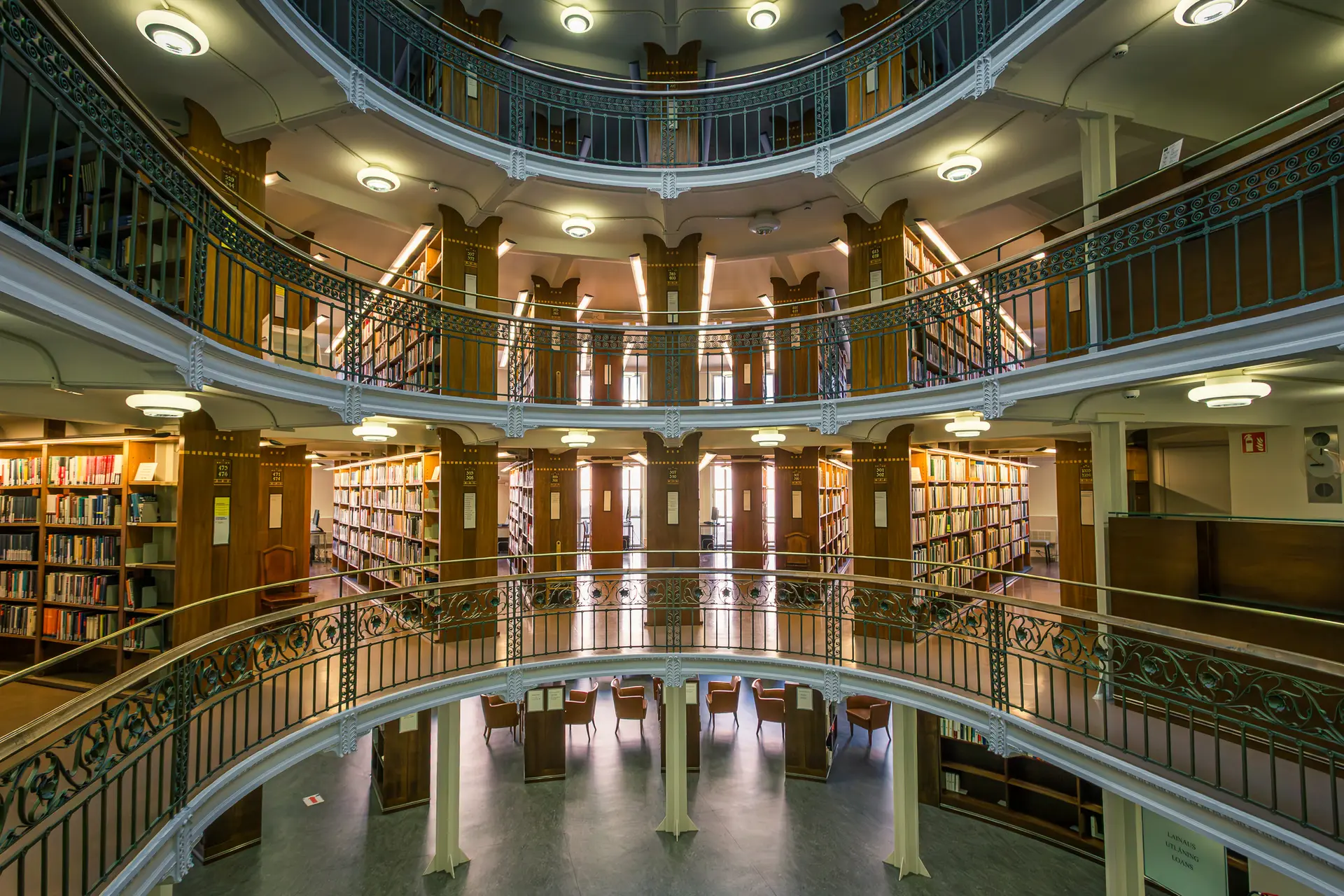 Historische Bibliothek mit mehreren Etagen, eleganten Geländern und Regalen voller Bücher. Helle Fenster lassen Licht herein.