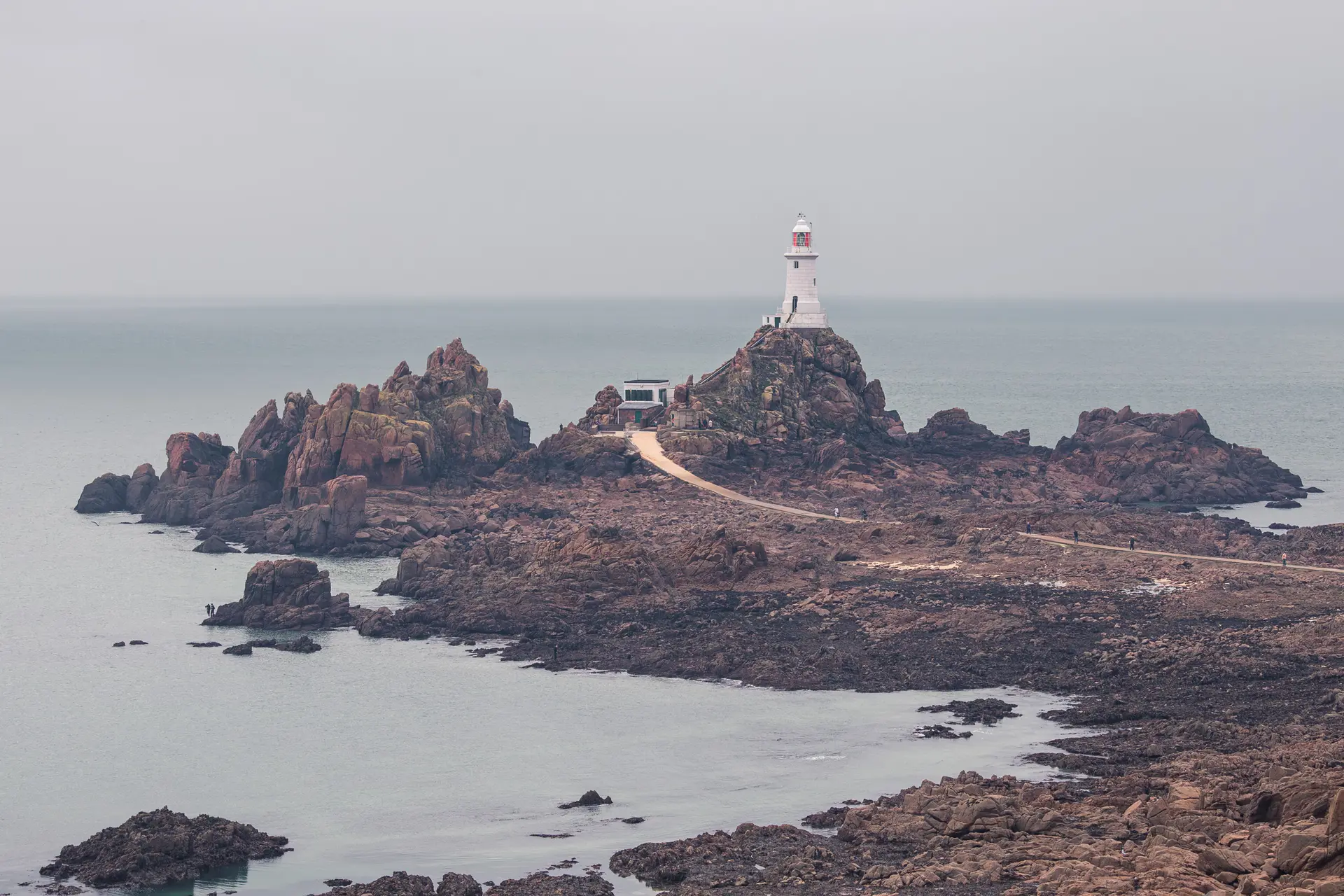 Leuchtturm auf felsiger Insel, umgeben von ruhigem Wasser. Die Strukturen sind in grauer Umgebung leicht sichtbar.