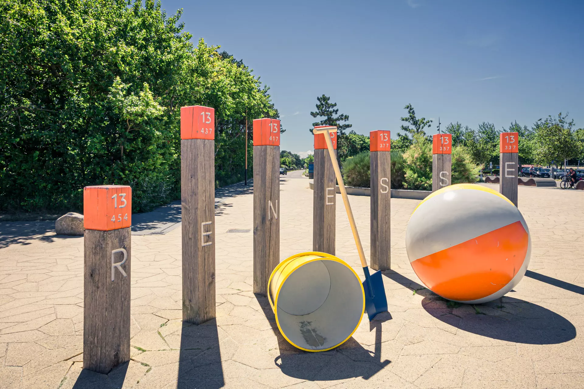 Wooden posts with orange numbers stand in a row, next to a large beach ball and a yellow toy.