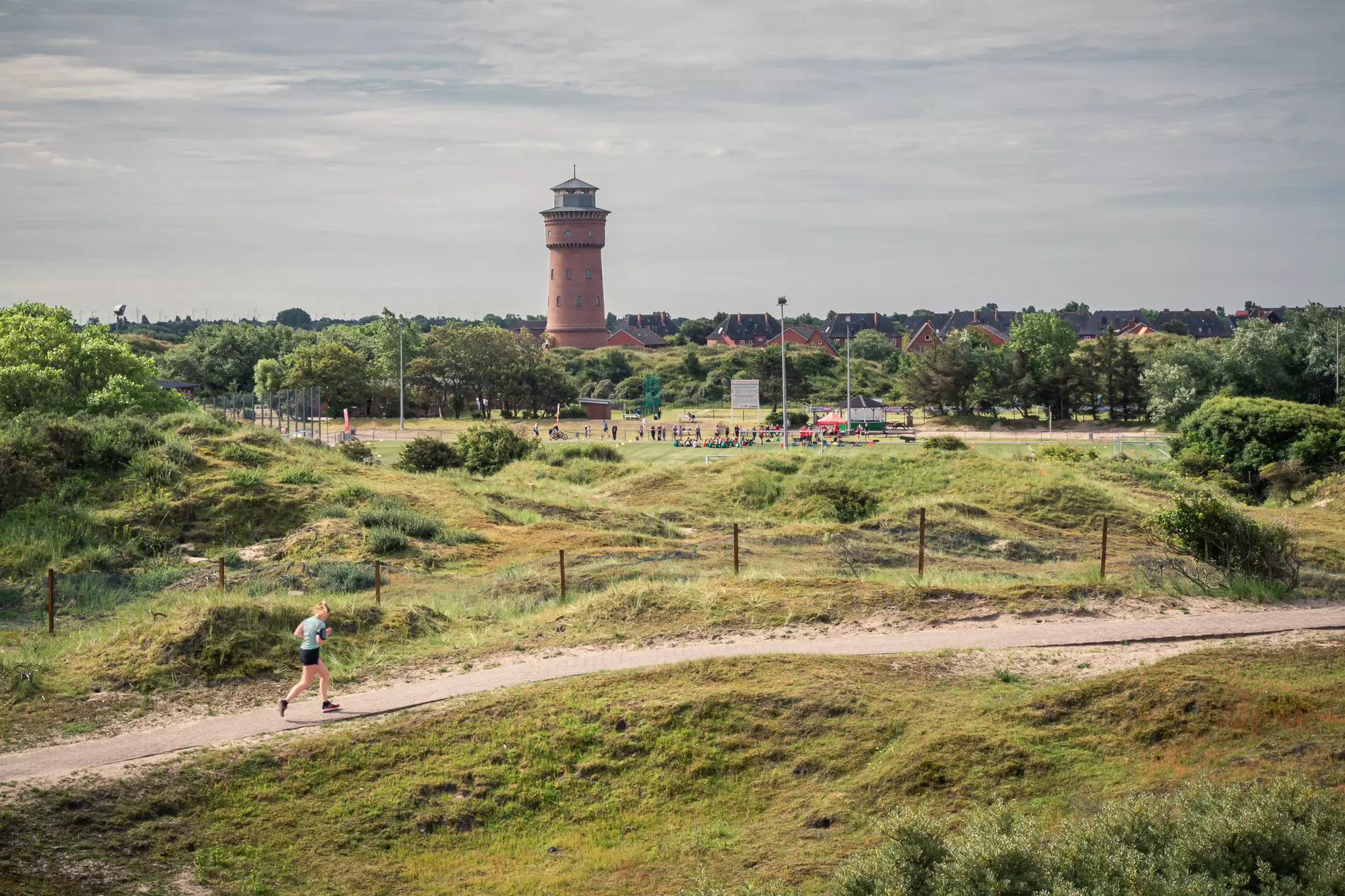 Jemand joggt durch die Dünenlandschaft von Borkum, im Hintergrund steht der alte Wasserturm.