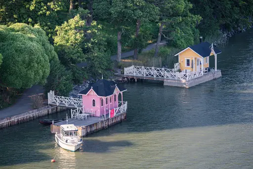 Bunte Holzgebäude am Wasser mit Boot und Holzstegen, umgeben von grünen Bäumen.