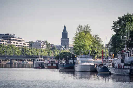 Boote am ruhigen Wasser mit grünem Ufer und sehenswertem Gebäude im Hintergrund. Ein klarer Himmel und sanfter Sonnenschein beleuchten die Szenerie.