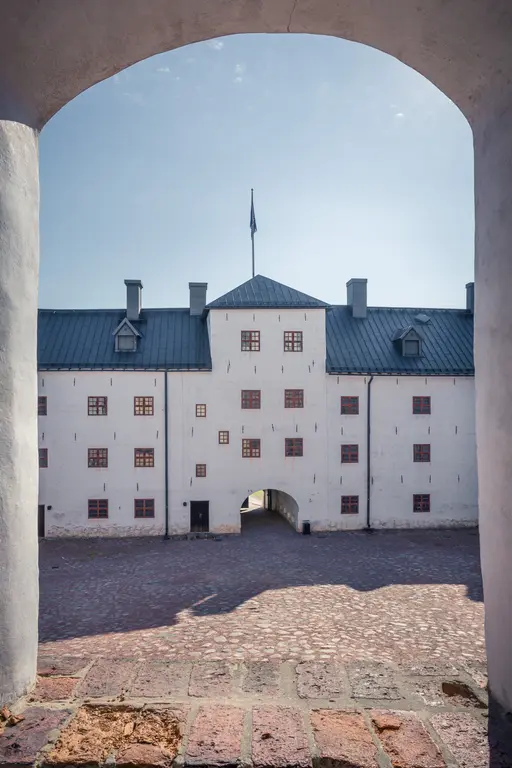 Blick auf den Innenhof eines historischen Gebäudes mit weißen Wänden und roten Fenstern, umrahmt von einem gewölbten Tor.