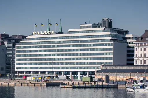Modern hotel building with "PALACE" sign, surrounded by water and docks, showcasing Helsinki's waterfront architecture.
