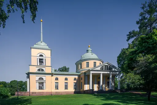 Stattliches Gebäude mit einer runden und einer rechteckigen Bauform, grünem Dach und goldenen Verzierungen, umgeben von Grünflächen.