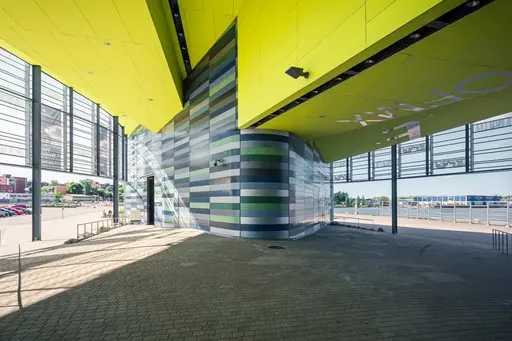 Moderne Architektur mit buntem, schräg gestellten Wänden und einer leuchtend gelben Decke. Große Fenster lassen viel Licht herein.
