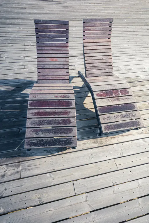 Zwei gestreifte Liegen aus Holz stehen auf einem hellen Holzdeck. Die Oberflächen sind verwittert und zeigen abgenutzte Stellen.