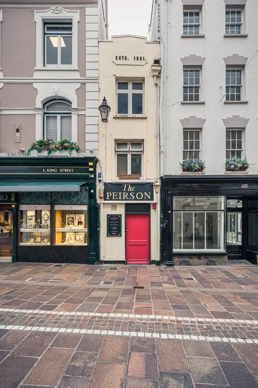 Belebte Straßenszene mit schmalem Gebäude und roter Tür, umgeben von unterschiedlichen Geschäften und historischen Fassaden.