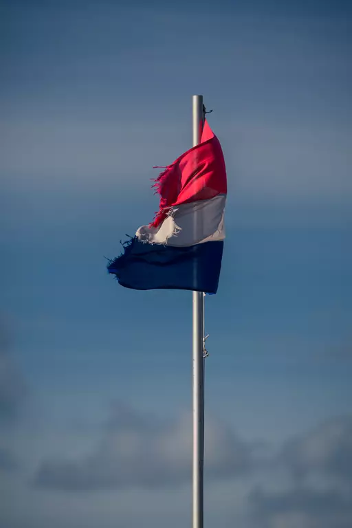 Eine zerrissene Flagge mit rot-weiß-blauen Streifen weht sanft im Wind an einem hohen Flaggenmast.