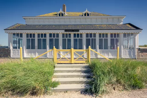 A white historic building with a black roof, surrounded by green grass and a yellow wooden gate.