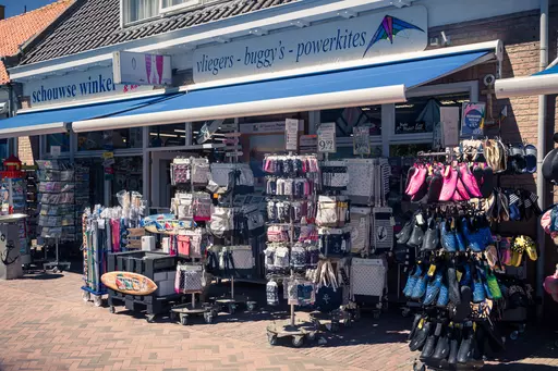 A shop with colorful displays of kites and accessories. In front are flyers, vibrant kites, and clothing items in various colors.