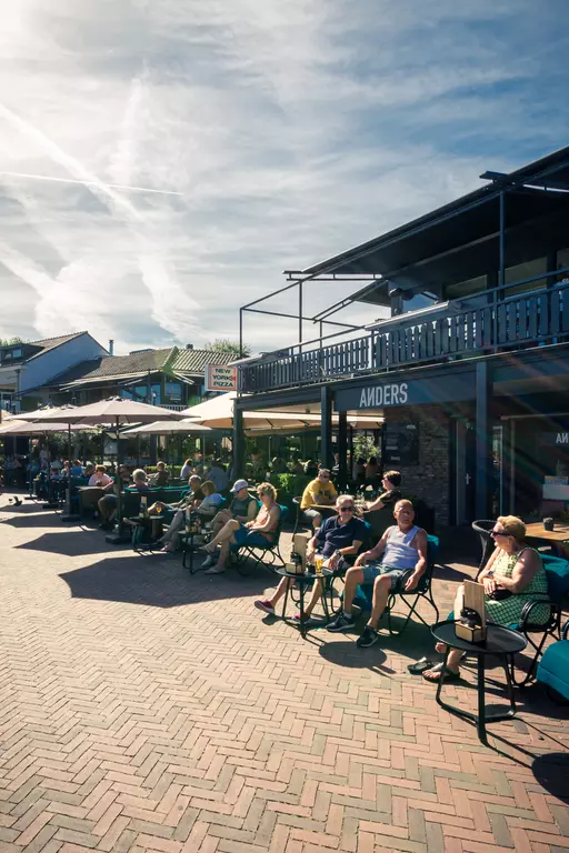 People sit in chairs outside a restaurant under sun umbrellas, chatting and laughing with one another.