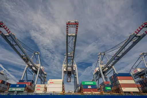 Large port cranes lift containers against a clear sky, surrounded by stacked containers on a cargo ship.