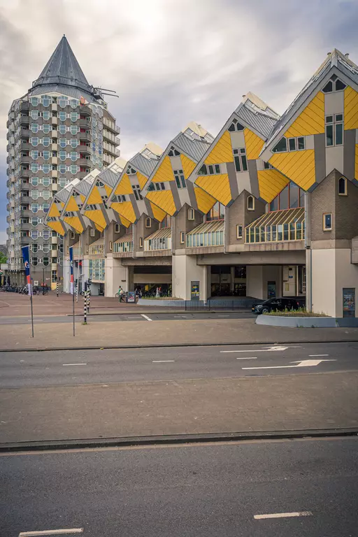 The image shows several yellow cube houses with slanted roofs, alongside a modern high-rise building.