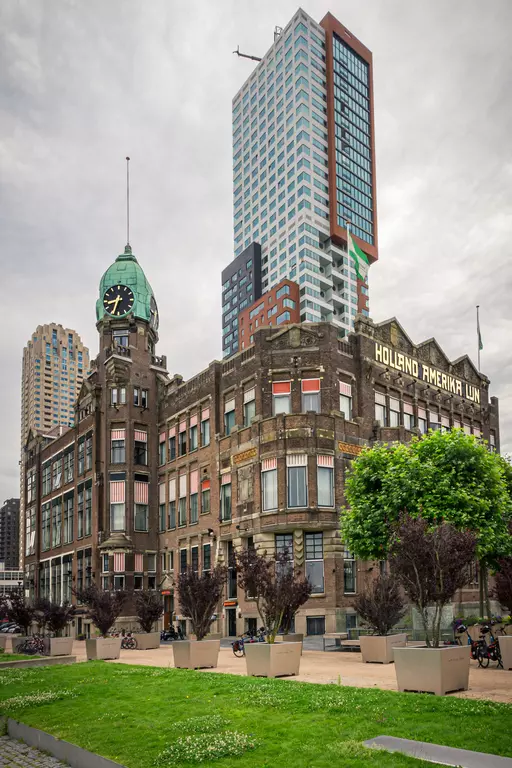 A historic building with a green clock tower peak, surrounded by modern skyscrapers and landscaped squares.