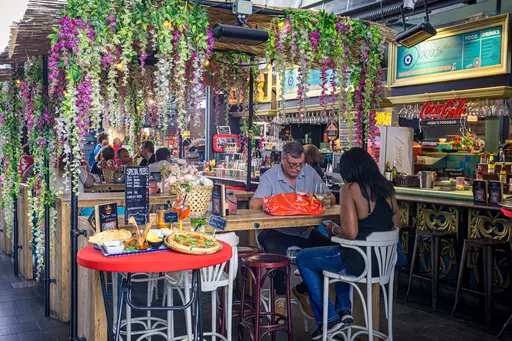 A lively dining scene with decorative flowers, tables, and guests enjoying food and engaging in conversation.