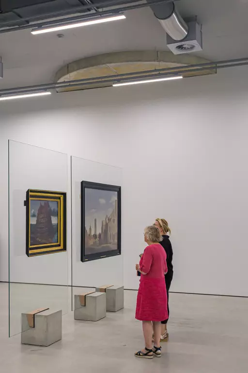 Two people are admiring paintings displayed on glass walls in a modern exhibition space with a minimalist design.