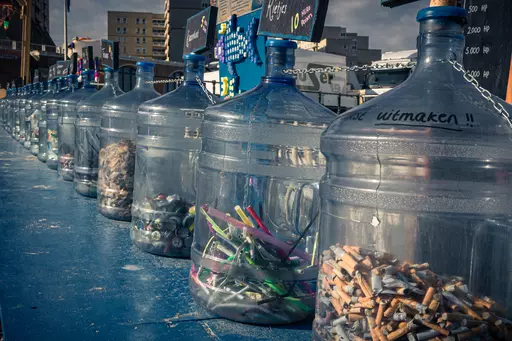 Transparent containers are lined up on a blue table, filled with various colorful materials and recycling items.