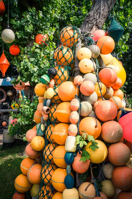 Bojeanhäufung auf Texel: Eine bunte Ansammlung von verschiedenen gelben, orangefarbenen und grünen Bojen hängt an einem Baum.