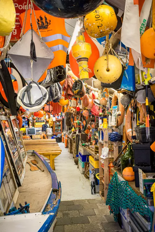 Boote und Fischereizubehör auf Texel: Ein schmaler Gang voller farbiger Bojen, Helme und anderer Ausrüstungsgegenstände.