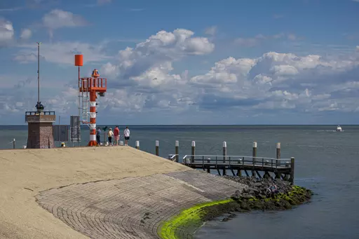 Seezeichen auf Texel: Ein rot-weiß gestreiftes Seezeichen steht an einem Sanddamm, während Menschen die Aussicht genießen.