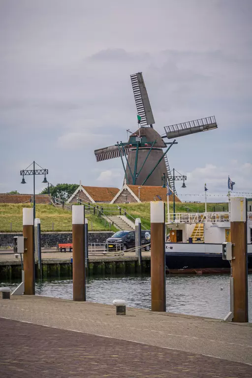 Windmühle auf Texel: Eine traditionelle Windmühle steht am Wasser, mit einem kleinen Hafen und Booten im Vordergrund.