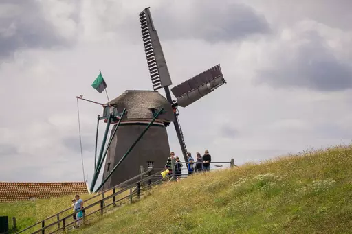 Windmühle auf Texel: Eine grüne Windmühle auf einem Hügel, umgeben von Besuchern und Wiese, mit typisch niederländischem Himmel.