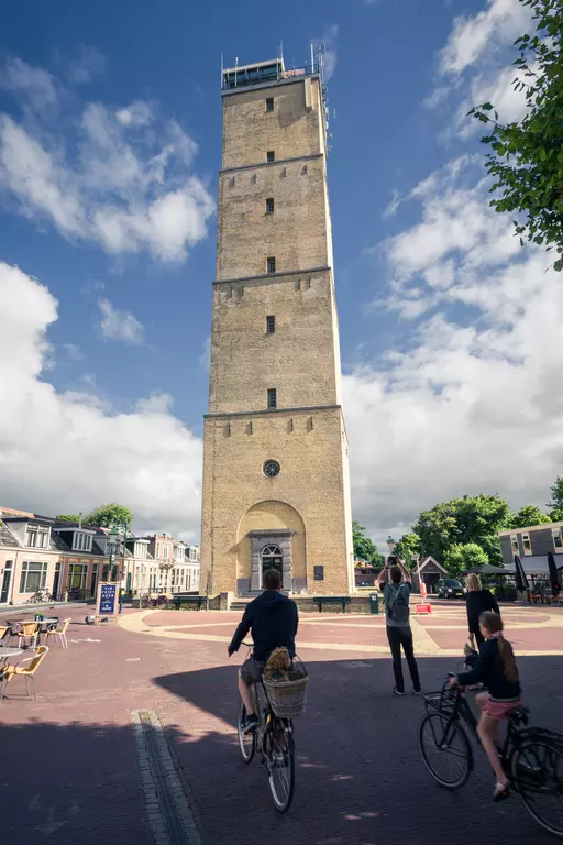 Leuchtturm Brandaris auf Terschelling: Ein hoher, historischer Leuchtturm umgeben von Radfahrern und niedrigen Gebäuden.