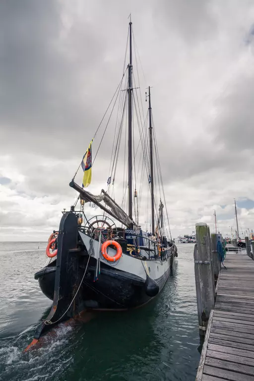 Schiff im Hafen von Terschelling: Ein historischer Segler mit mehreren Masten und orangefarbenen Rettungsringen am Bug.